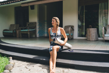 Relaxed barefoot woman sits with yoga mat and smartphone nearby, symbolizing tech-enabled wellness,...