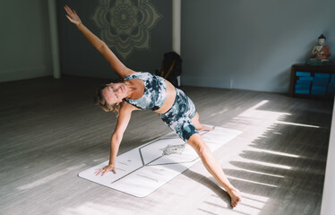 Blonde woman smiling during side plank variation, holding strong arm balance on yoga mat, radiating...