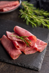 Sliced beef pastrami on cutting board on black table.