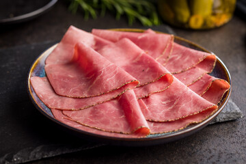 Sliced beef pastrami on plate on black table.