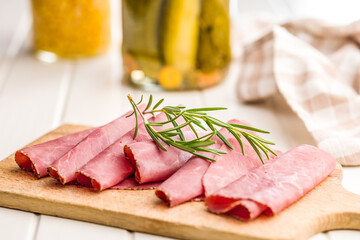 Sliced beef pastrami on cutting board on white table.