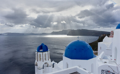 Scenic view of blue-domed churches in Oia, Santorini, Greece under dramatic cloudy sky with sun...