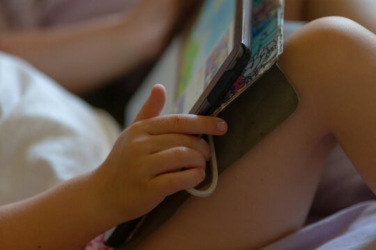 A young child is happily reading a colorful book while comfortably laying on a cozy bed, immersed in the imaginative story within