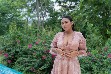 Fashion model posing in a garden setting, wearing a stylish pink dress