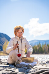 Woman performing a sound ritual with a Tibetan singing bowl by the Altai river. Concept of feminine...