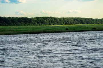 A calm river reflects the soft light of the setting sun, framed by vibrant green hills and...