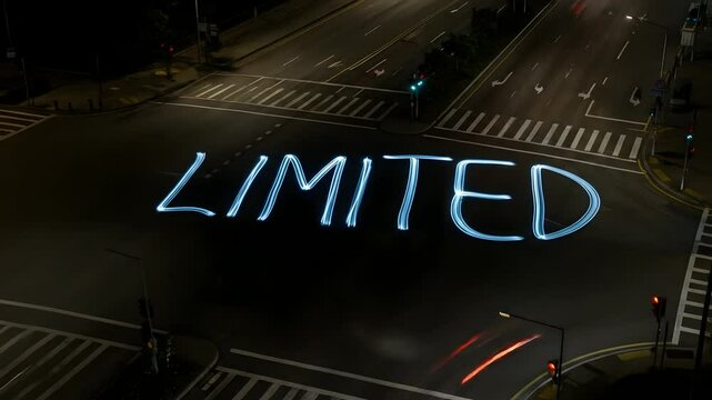Traffic at night forms light trails around 'LIMITED' word art at intersection, challenges, business concept, scarcity marketing, time lapse. Urban development or city planning use.