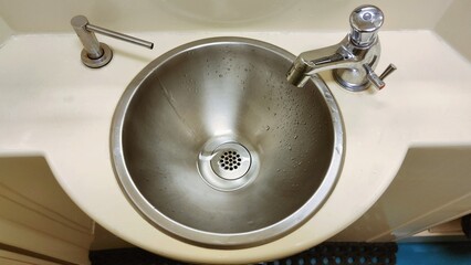 Washbasin in bathroom of railway carriage. Metal sink, hot and cold water faucet and liquid soap...