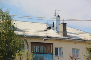 Black and White Sneakers Hanging by Laces from Overhead Wires with Building, Chimney, and Trees in the Background