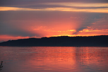 Tranquil Sunset Over Calm Water with Vibrant Orange and Purple Sky Reflections and Dock Extending Toward Tree-Lined Horizon