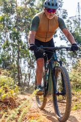 Senior man riding electric mountain bike uphill on a trail