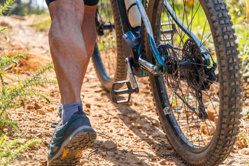 Naklejka premium Senior cyclist pushing his electric mountain bike uphill on a dirt road
