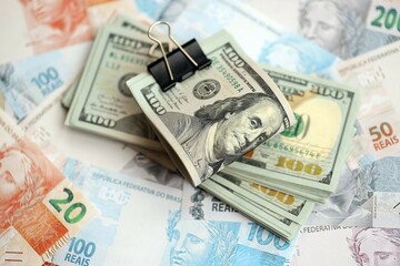 Bunch of US dollar bills lies on big amount of Brazilian reais banknotes close up