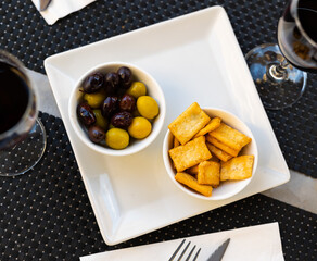 Black-and-white contrasting background, snacks are prepared on table - green and black olives with...