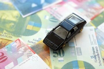Swiss franc banknotes and toy car. The current francs money bills and black car lies on table