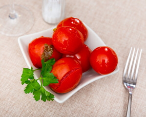 There is bowl of pickled tomatoes with parsley on table, traditional Italian appetizer for hearty lunch..
