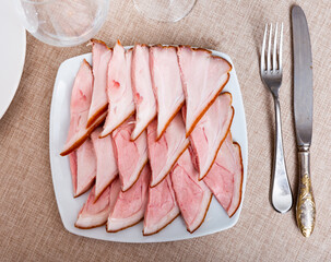 Thin slices of smoked fore hock are laid out on flat plate, treat for guests, addition to strong alcohol beverages and dinner dish. Pink slice of meat delicacy, top view.