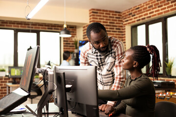 Bearded manager stands by the desk engaging in creative discussion with a female employee at the...