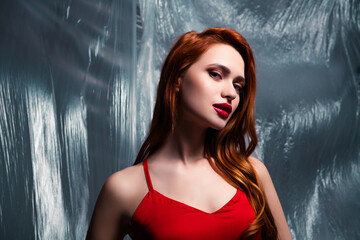 Portrait of a young woman with red hair in stylish red dress under artistic lighting with...