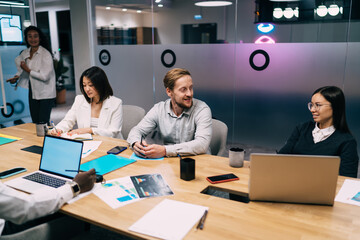 Diverse group of businesspeople collaborating in evening office session, using laptops and notes to drive project strategy with strong focus on innovation, teamwork, and digital tools