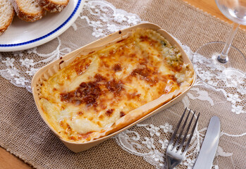 On wooden table traditional Italian dish is lasagna baked in oven under cheese crust