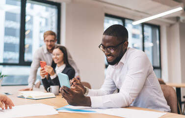 Smiling African-American businessman engaging with smartphone during team work session in bright...