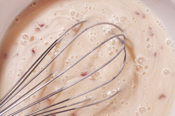 Protein cocktail pink colored with berry pieces. The process of making a cocktail with a steel whisk