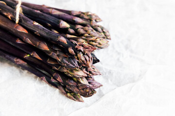 Fresh purple asparagus tied with twine on white textured background ready for cooking