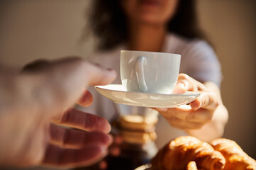 A person extends a coffee cup in a gesture of sharing during breakfast, alongside croissants on a...