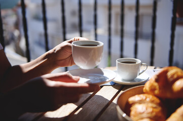 A serene moment enjoying coffee and croissants on a sunlit balcony with blurred urban scenery in the background. Perfect for concepts like relaxation, breakfast, and outdoor leisure.