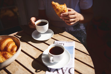 Table setting with coffee, croissants, and a magazine, portraying a peaceful morning routine in natural sunlight.