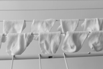White baby socks neatly hanging on a drying rack indoors, arranged in rows, black and white minimalist photo, concept of parenting and cleanliness