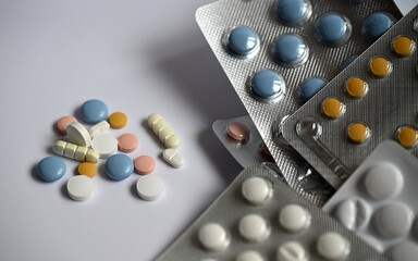 Assorted colorful pills and tablets, both loose and in blister packs, arranged on a neutral white...