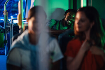 Young man wearing earbuds smiling while riding bus at night