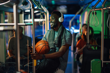 Smiling basketball player wearing headphones and holding ball on bus