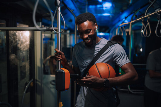 Smiling basketball player using smartphone on bus at night - Powered by Adobe