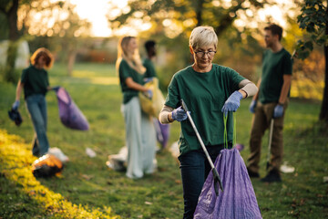 Senior woman picking up trash with volunteers in the park