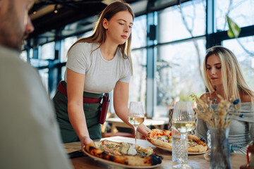 Young waitress carefully placing a gourmet pizza on the table for customers in a modern restaurant