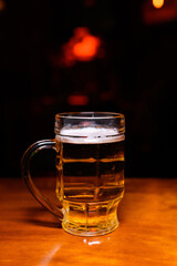Pint of light beer in a glass mug on a wooden bar counter. Warm lighting and dark background create a cozy pub atmosphere