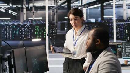 Fototapeta premium Happy data center manager providing positive feedback to engineer developing neural networks software on computer. Cheerful supervisor pleased by employee work implementing AI in server room, camera A