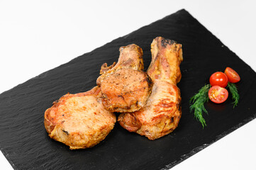 Three roasted bone-in pork chops with a golden crust are arranged on a black slate tray. Garnished with halved cherry tomatoes and sprigs of fresh dill