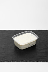 A plastic container filled with thick white sauce with herbs stands on a black slate plate. The creamy and refreshing sauce pairs well with meat, fish, or vegetables