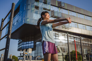 Japanese woman in a sportswear stretching in park before workout