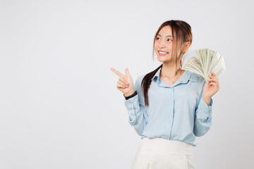 Obraz premium Happy Asian woman point at Empty space while holding money fan banknotes, dollar money shining in hand, symbolizing luck and success in finance and wealth management. isolated studio white background