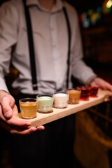Waiter serves six colorful shots on a wooden tray. The cocktails are arranged in a row, creating a striking contrast. Bar atmosphere, party vibe, and stylish presentation