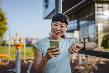 Japanese woman in a sportswear stand in park and use mobile phone