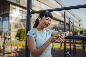 Japanese woman in a sportswear stand in park and use mobile phone