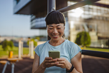 Japanese woman in a sportswear stand in park and use mobile phone