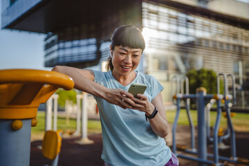 Japanese woman in a sportswear stand in park and use mobile phone