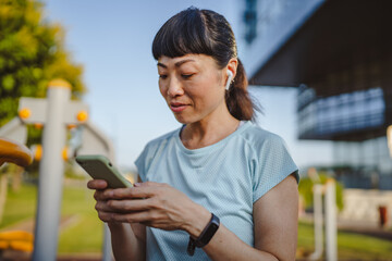 Japanese woman in a sportswear stand in park and use mobile phone